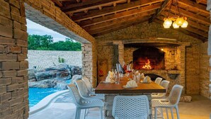 An outdoor dining area with a brick fireplace, a pool, and white wicker chairs. - 8 bedroom beautiful home in Zaton (Zaton)