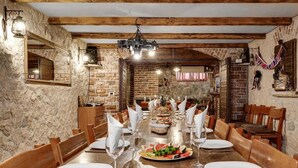 A dining area with a long wooden table set for a meal, stone walls, and a hanging light fixture. - 8 bedroom beautiful home in Zaton (Zaton)