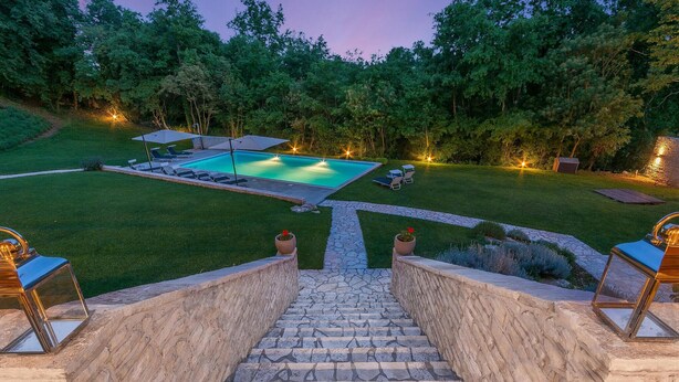 Uma escadaria de pedra leva a um quintal com piscina, rodeado por um gramado bem cuidado e árvores.
