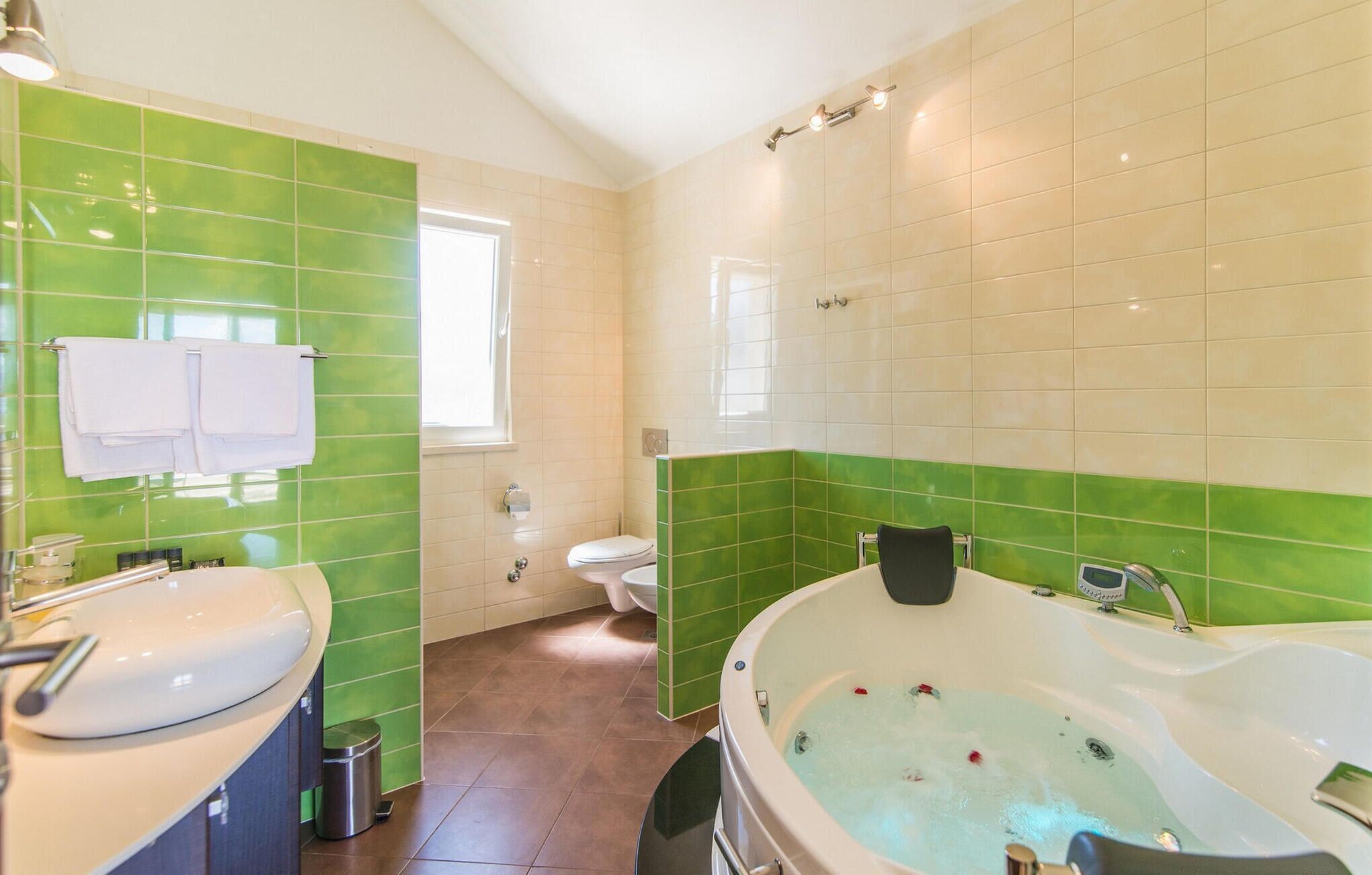 A bathroom with green and beige tiles, a bathtub, a toilet, and a sink.