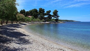 A pebble beach with clear water, trees, and a distant shoreline. - Beautiful home in Mirca (Mirca)