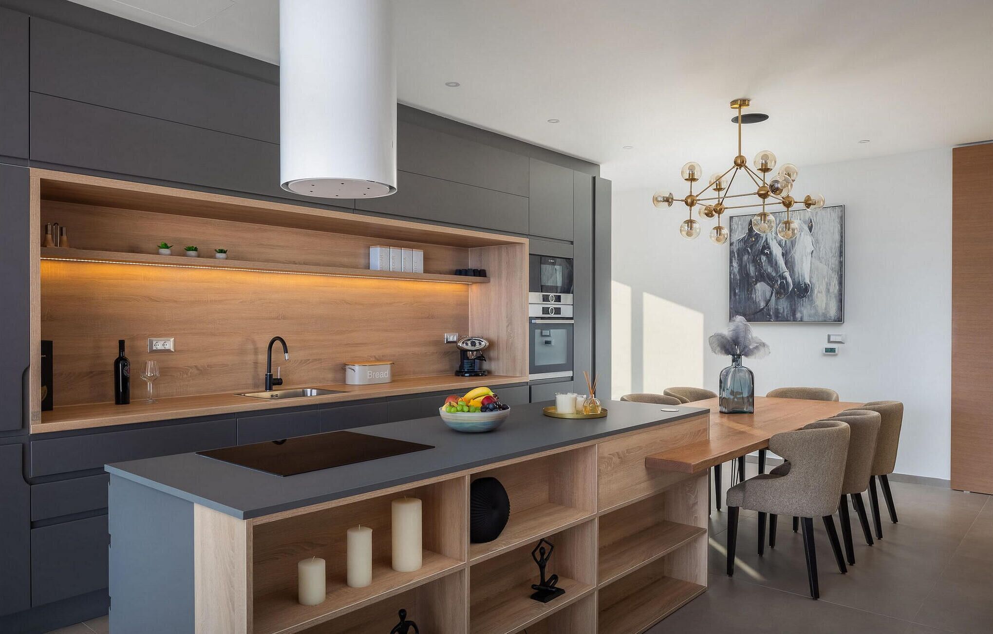 A modern kitchen with a central island, built-in oven, and a dining area with chairs.