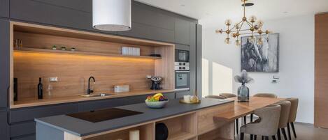 A modern kitchen with a central island, built-in oven, and a dining area with chairs.