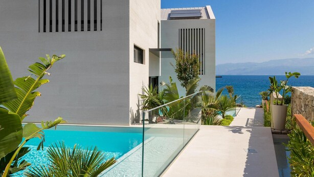 A modern pool area with a clear view of the sea, surrounded by tropical plants and a white building with a glass barrier. - Stunning home in Sutivan with sauna (Sutivan)