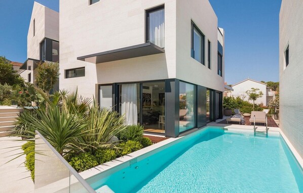 A modern two-story house with a swimming pool, large windows, and a well-maintained garden.
