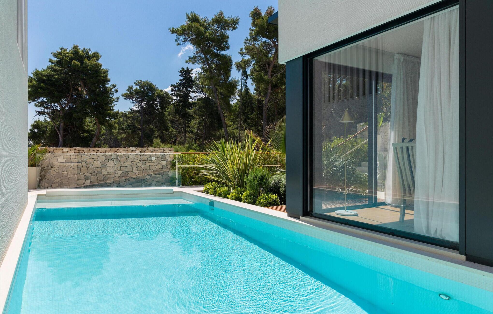 Una piscina moderna amb una paret de pedra i vegetació abundant al fons.