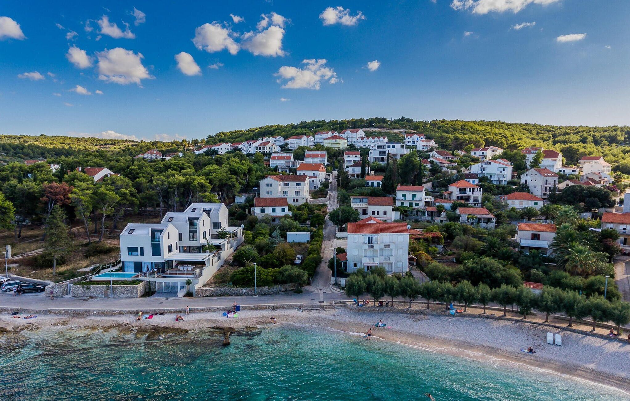 A coastal town with white buildings, a beach, and clear blue waters.