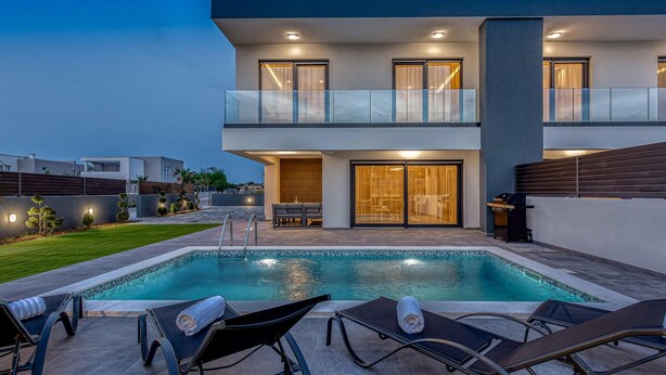 Ein modernes, zweistöckiges Haus mit Pool, Sitzgelegenheiten im Freien und einer gut beleuchteten Eingangsparte.