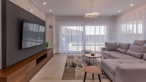 Ein modernes Wohnzimmer mit einem an der Wand befestigten Flachbildfernseher, einem grauen Sofa, einem Couchtisch und einem gemusterten Teppich.