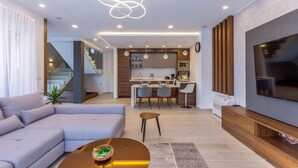 Ein modernes Wohnzimmer mit einer Couch, einem Couchtisch und einem Fernseher. Es gibt eine Küchenzeile mit einem Esstisch und Stühlen sowie eine Treppe, die zu einer oberen Etage führt.