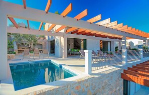 Relax by the pool surrounded by a pergola and stone wall.