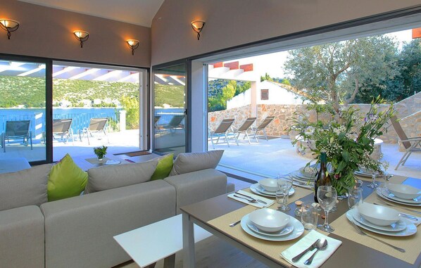 Relax in a serene room with a large window overlooking an outdoor seating area, featuring a sofa, dining table, and lounge chairs.