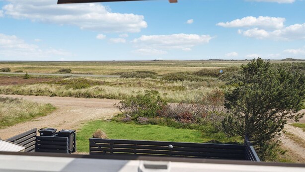 A view from a window overlooking a grassy field with a dirt path and a bench.