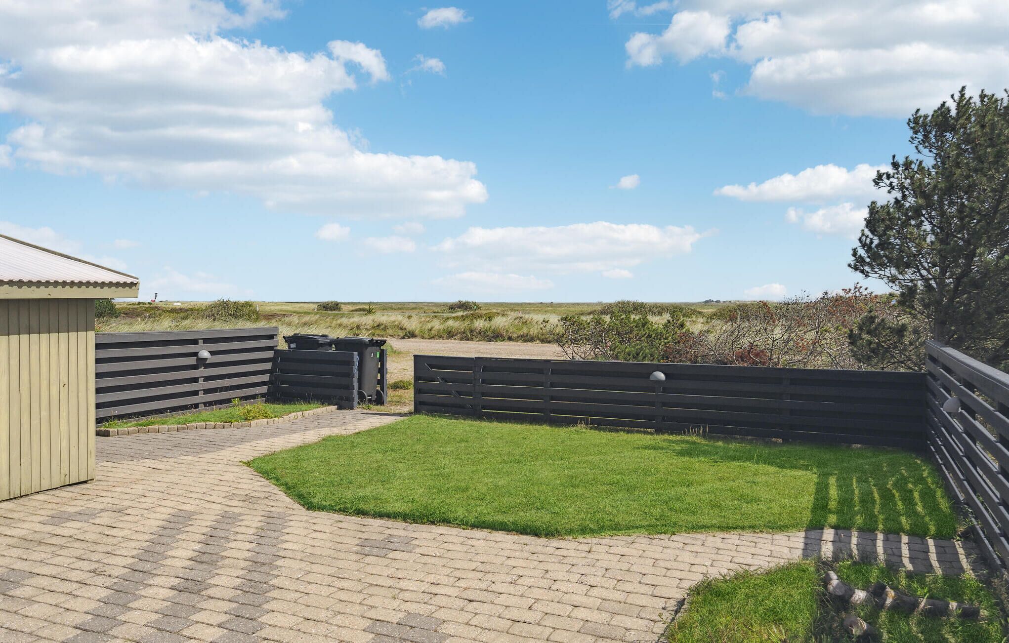 En anlagt terrasse med græsplæne, et træhegn og en bygning med skrå tag.