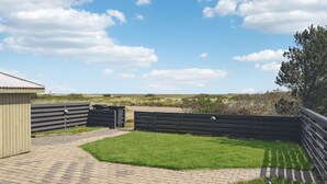 A paved patio with a grassy lawn, a wooden fence, and a building with a sloped roof.