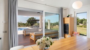 A modern living room with a wooden dining table, a sofa, and a view of an outdoor swimming pool and garden. - Luxurious home in Svetvincenat (Svetvincenat)