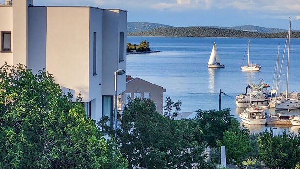 Un puerto deportivo con veleros, un edificio moderno y un mar tranquilo.