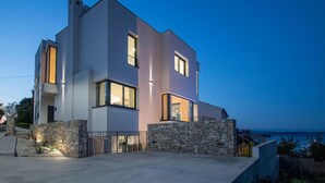 Una casa moderna de dos pisos con fachada de piedra, ventanas amplias y vista al mar.