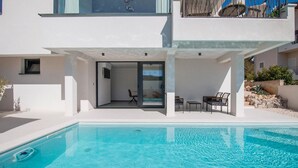 Una casa moderna con piscina, un porche cubierto con mobiliario y una puerta de vidrio que da a un espacio interior.