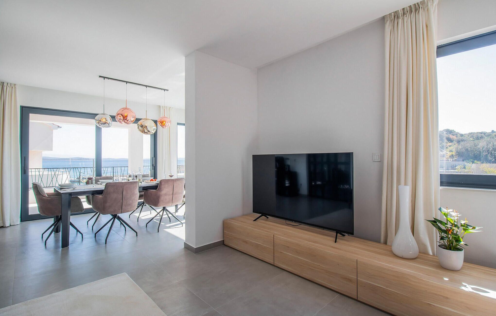 Un saló modern amb un televisor de pantalla plana, un moble de roba per a l'aparell d'àudio, zona de menjador amb cadires roses i un balcó amb vistes.