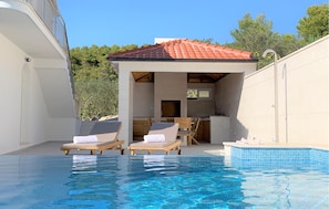 A pool area with lounge chairs, a covered seating area, and a tiled roof.