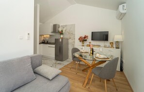 Una cocina moderna con salpicadero de mármol, un comedor con mesa de vidrio, sofá tapizado en gris y un televisor de pantalla plana montado en la pared.