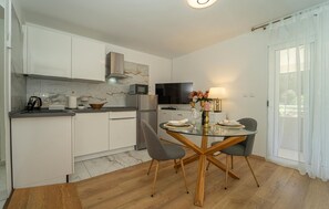 Una cocina moderna con armarios blancos, salpicadero de mármol, horno empotrado y comedor con mesa y sillas de vidrio.