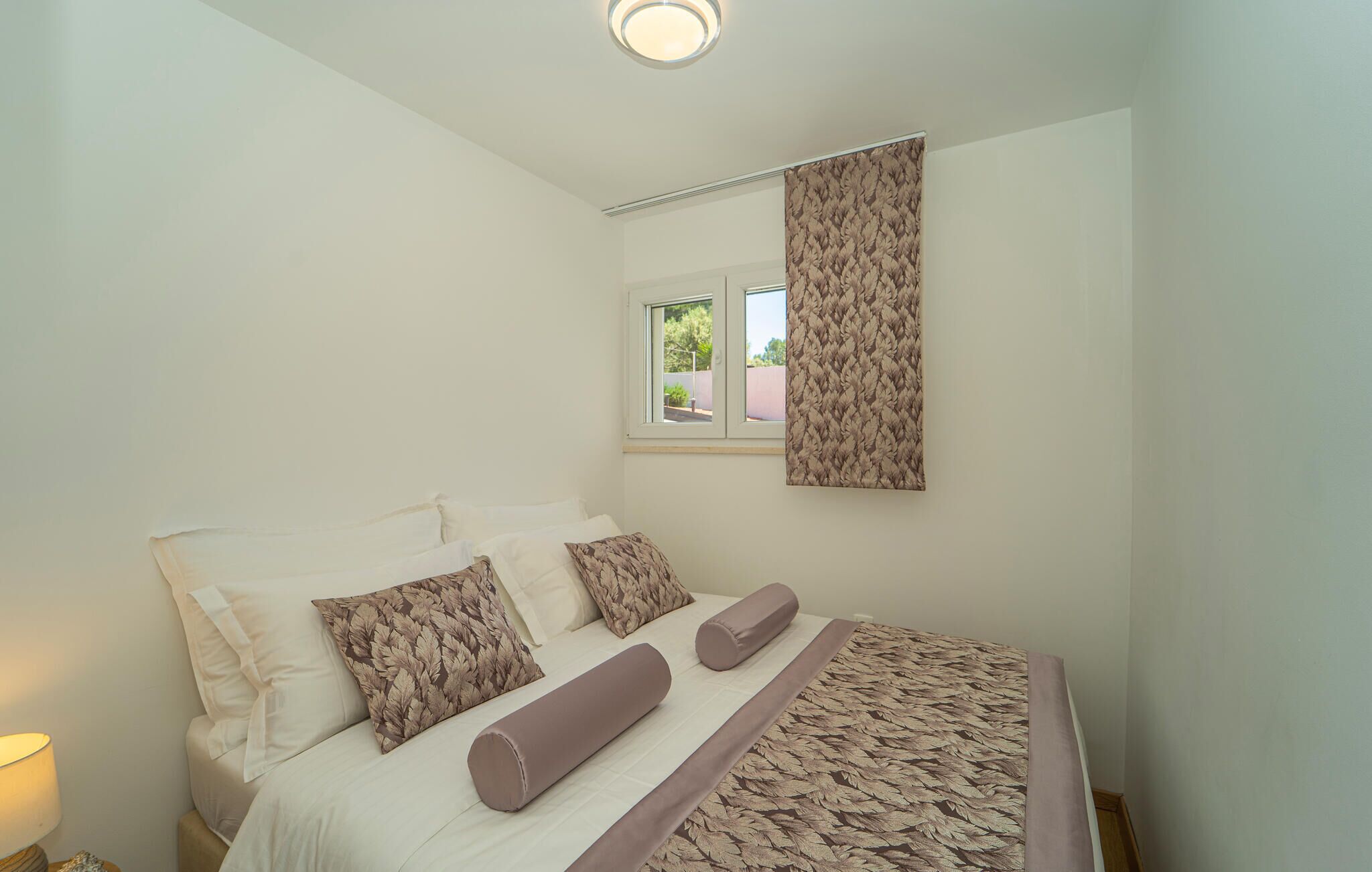 Um quarto com cama, almofadas, janela e cortina.