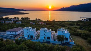 Une zone côtière avec des bâtiments modernes, une vue dégagée sur le coucher de soleil sur la mer et un paysage vallonné en arrière-plan.
