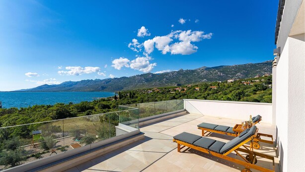 Un balcon avec vue sur la mer et les montagnes, aménagé avec deux chaises longues et une table.