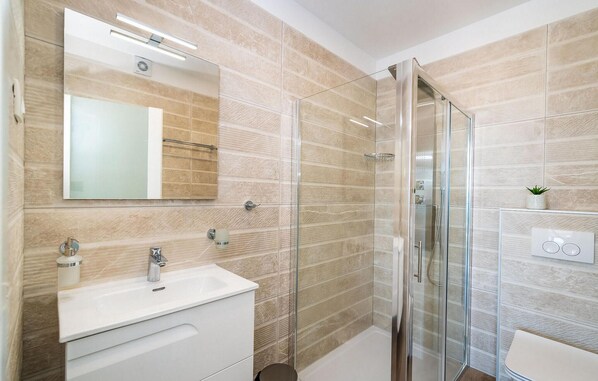 Un baño moderno con cabina de ducha de vidrio, un lavabo blanco y un espejo grande.