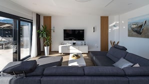 Un salon moderne avec une grande télévision, des canapés gris, une table basse et une plante en pot.