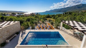 Une piscine avec des chaises longues, un mur en pierre et une vue sur la mer et les montagnes.