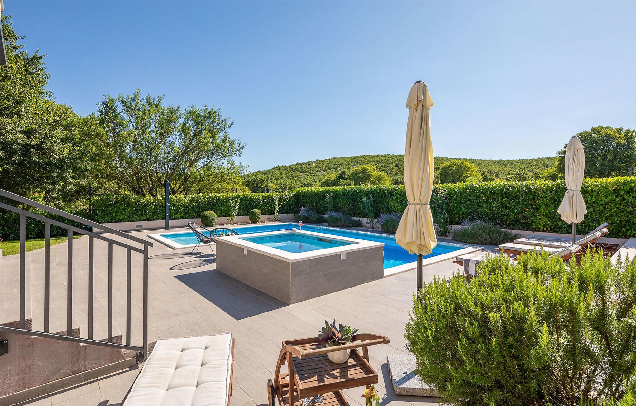 Ein Poolbereich mit rechteckigem Pool, Liegestühlen und Sonnenschirmen.