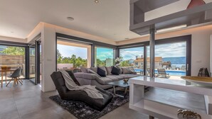 Ein modernes Wohnzimmer mit einer Eckcouch, einem Essbereich und Blick auf einen Pool und Berge.