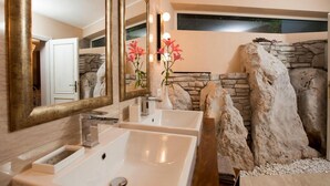 Un baño con un espejo grande, un lavabo blanco y una pared decorada con piedras.