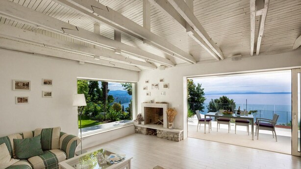 Amplia sala de estar con chimenea, sofá, una mesa de centro y comedor con vistas al mar.