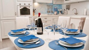 Una mesa de comedor con manteles individuales azules, platos blancos y copas de vino, con una botella de vino y una botella de agua sobre la mesa.