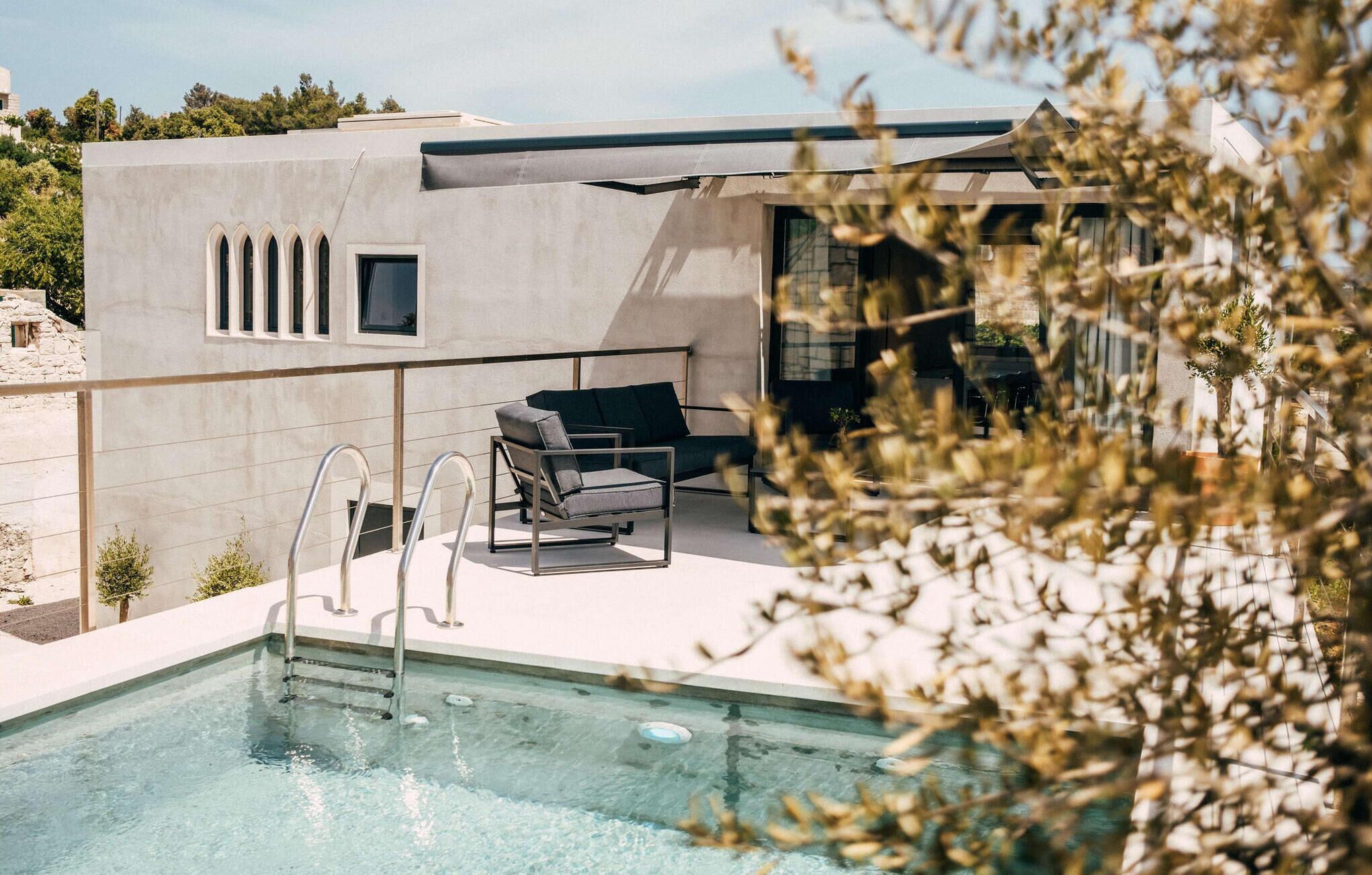Ett modernt utomhuspoolområde med en minimalistisk design, inklusive en pool, en sittgrupp med soffa och stolar samt en fri utsikt över det omgivande landskapet.
