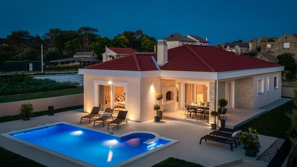 Una casa moderna con piscina, mobiliario exterior y chimenea.