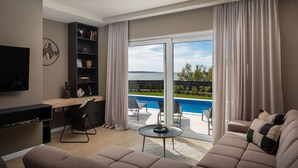 Una sala moderna con un televisor de pantalla plana, una estantería, un sofá, una mesa de centro y vistas a una piscina y zonas verdes.