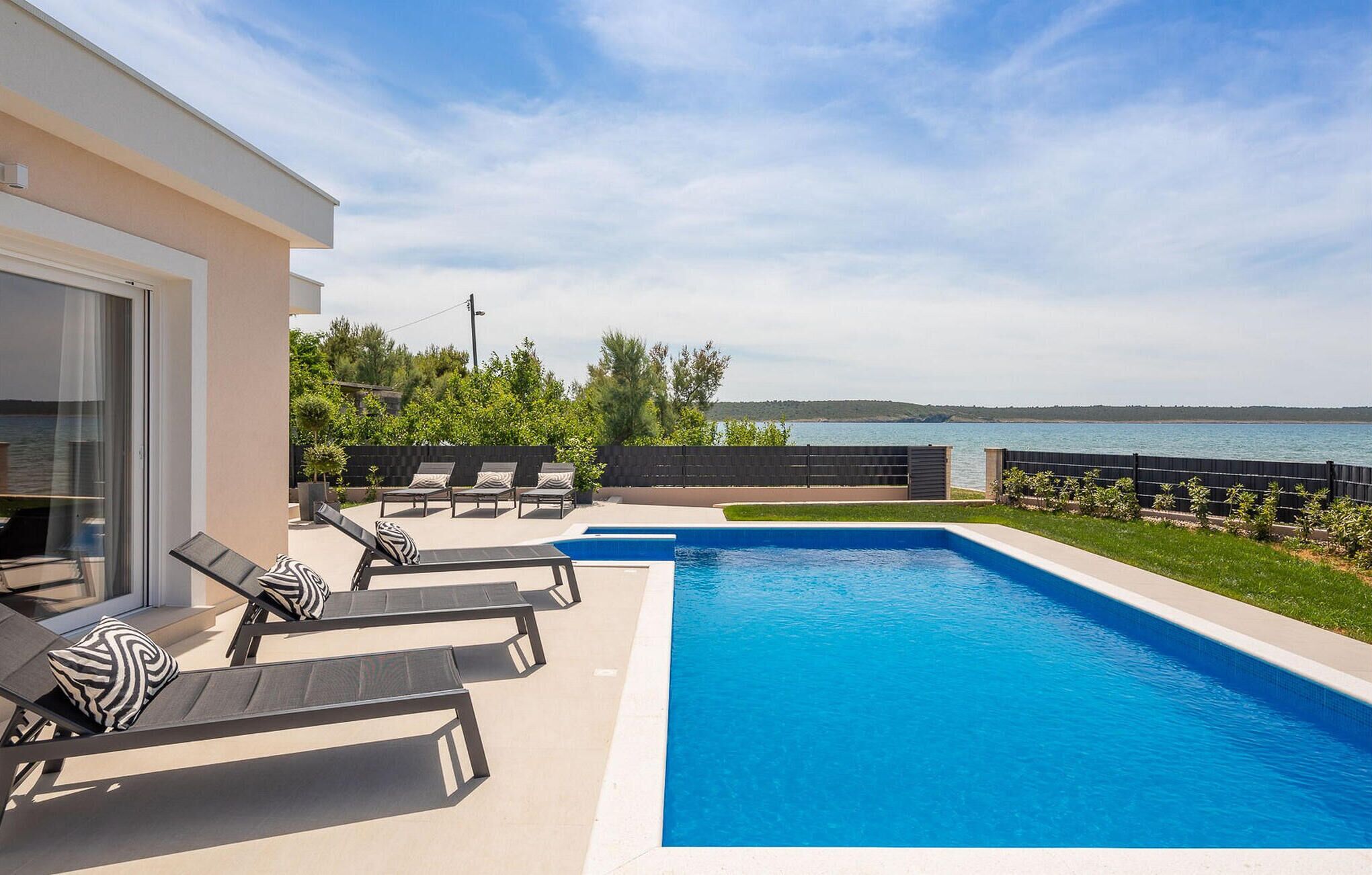 A modern outdoor pool area with lounge chairs and a view of the sea.