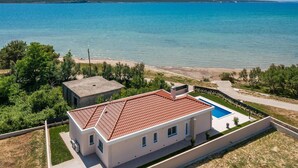 Una casa moderna de dos pisos con piscina, rodeada por un jardín ajardinado y vista al mar.