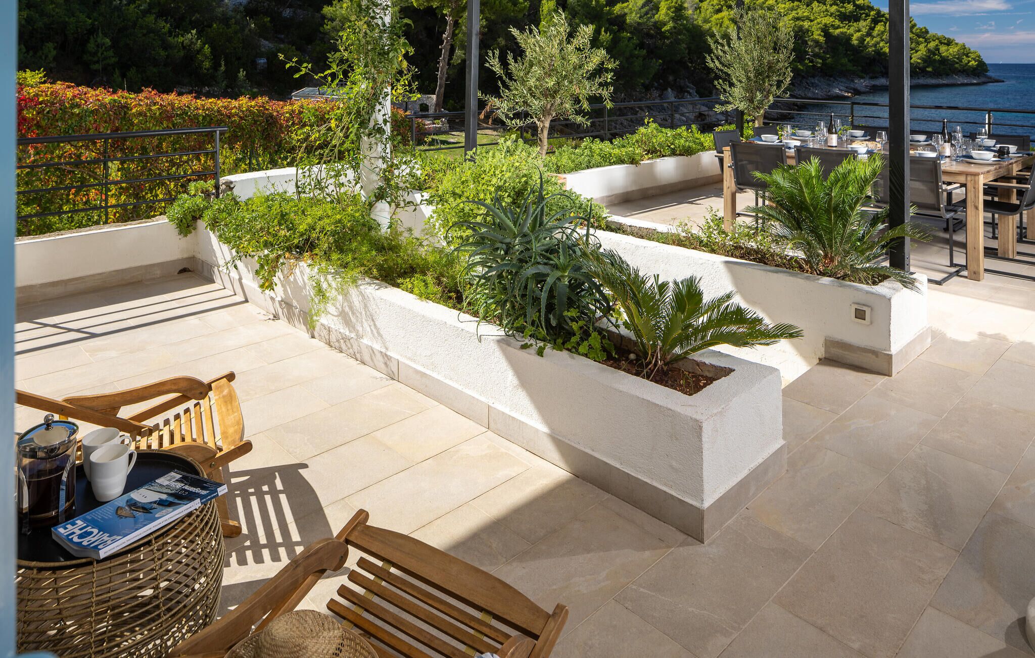 An outdoor patio with a dining table set, surrounded by planters and chairs.