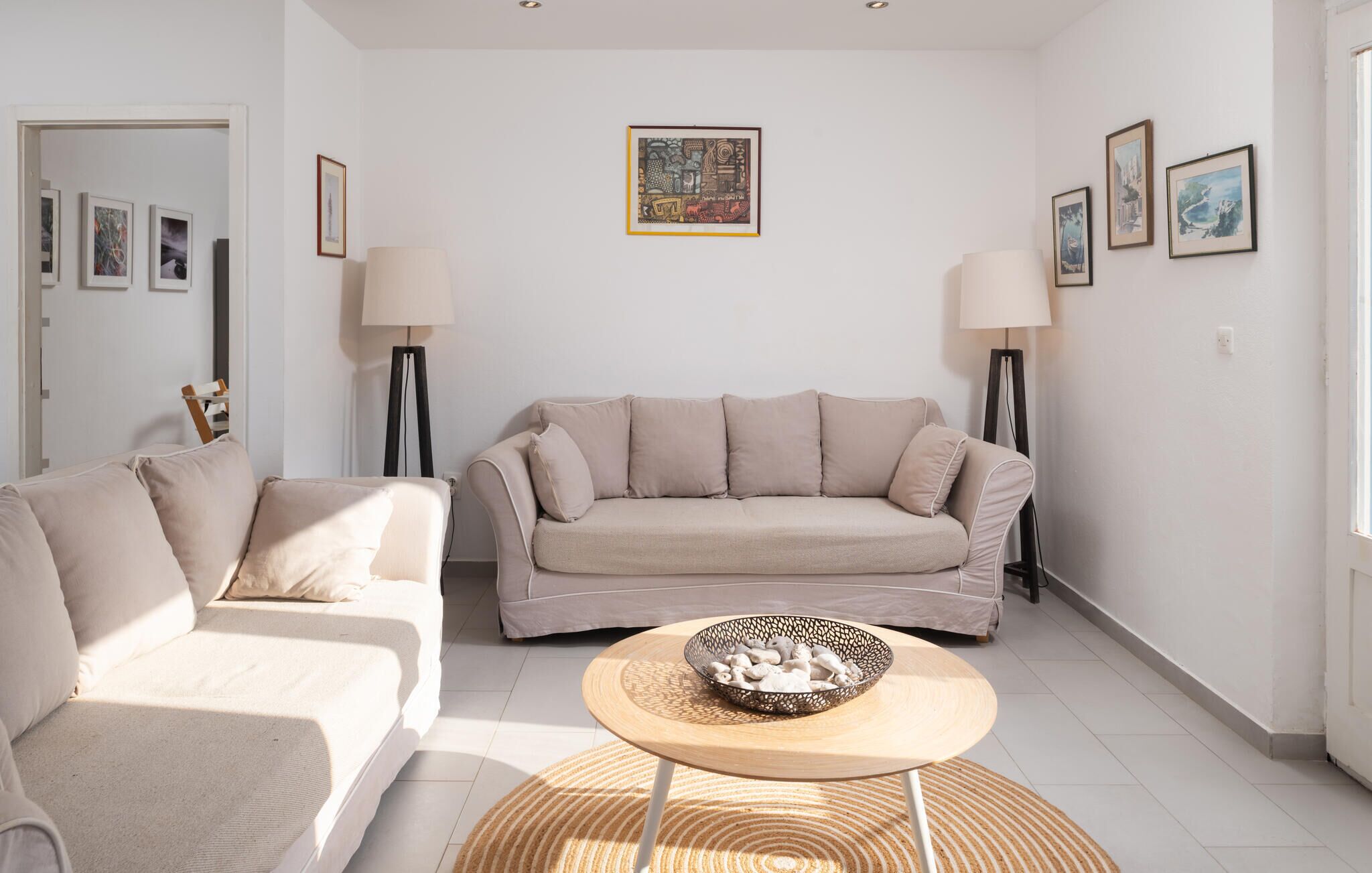 A living room with a beige sofa, a smaller sofa, a coffee table with a bowl, and two floor lamps.