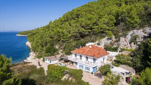 Ein Küstenhaus mit rotem Ziegeldach, umgeben von üppigen, grünen Bäumen und einem klaren, blauen Meer.
