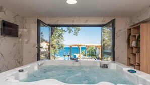 Ein Wellnessbereich mit Whirlpool und Meerblick durch offene Türen.