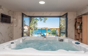 Relax in a spacious hot tub with a control panel, overlooking the sea and outdoor lounge area.