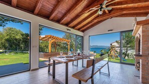 Ein Essbereich mit einem Holztisch und Bänken, große Fenster mit Blick auf Meer und Grün.