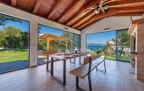 Enjoy expansive views of a lush garden and a body of water from the comfort of this room, featuring a dining table for six and a brick fireplace.